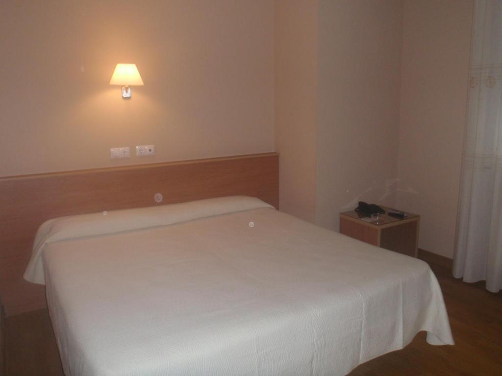 a bedroom with a white bed and a light on the wall at Hostal CC in Aranda de Duero