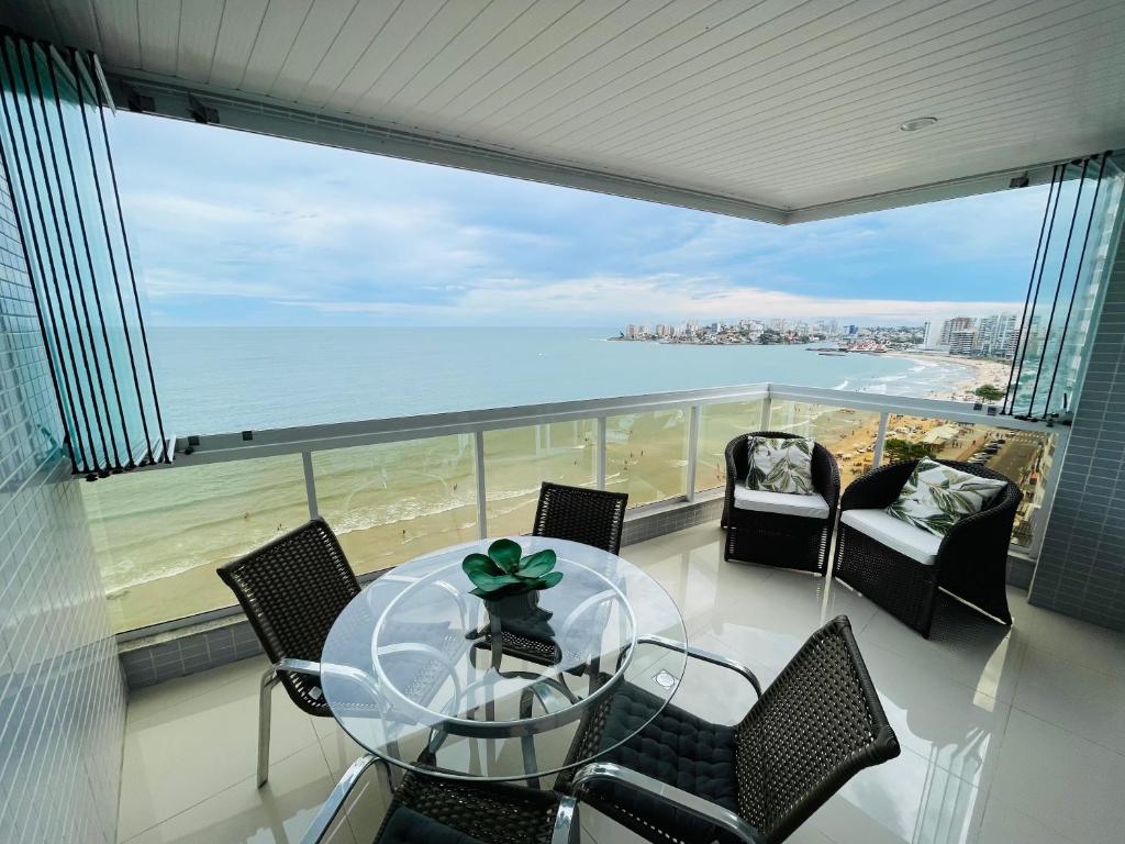 een balkon met een glazen tafel en stoelen en de oceaan bij praia do morro Guarapari,beira mar topíssimo apartamento in Guarapari