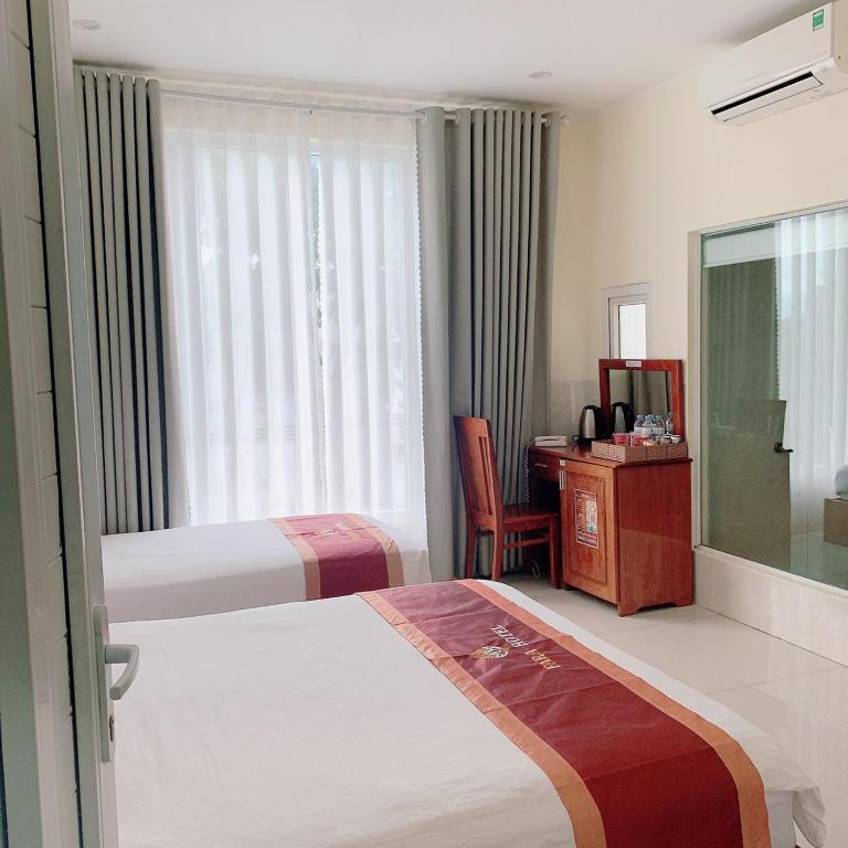 a hotel room with two beds and a desk and a window at Khách Sạn FARA in Phan Rang