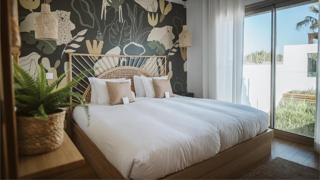 a bedroom with a large white bed with a plant at The Salty Pelican Yoga & Surf Retreat in Peniche