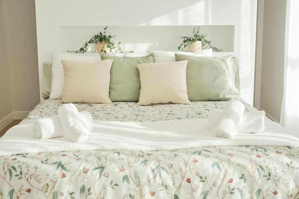 Una cama blanca con almohadas blancas y plantas. en CASA ROLAO Elegante Casa Familiar 10 personas, en Sierra de Outes