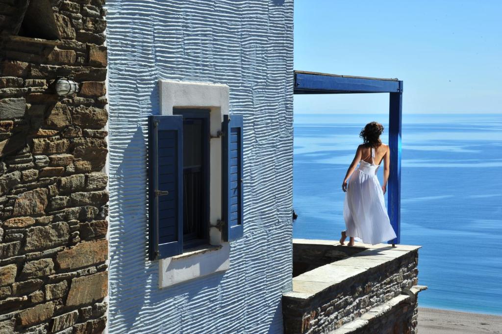 Una mujer con un vestido blanco está parada en una ventana en Aegea Blue Cycladic Resort, en Zorgos 