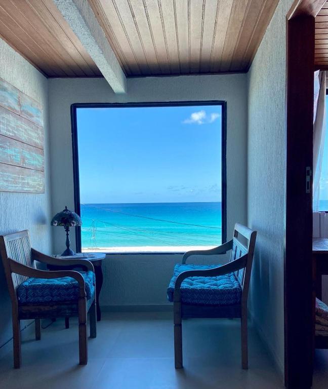a room with two chairs and a large window with the ocean at Pousada Casa do Telhado Verde in Cabo Frio