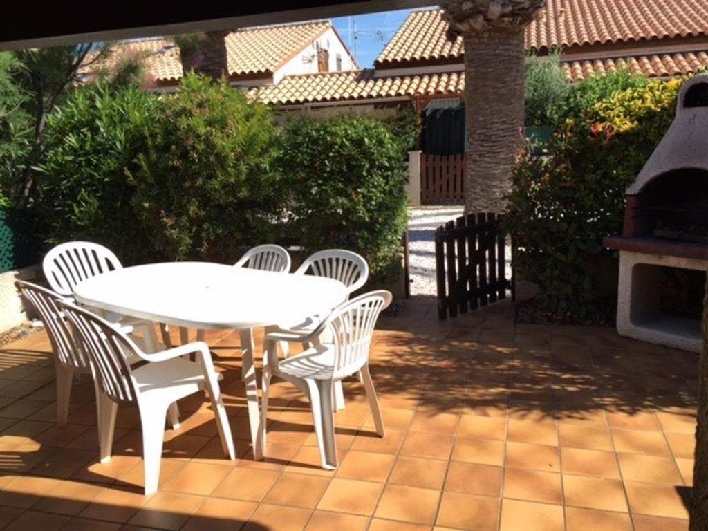une table et des chaises blanches sur une terrasse avec une cheminée dans l'établissement Villa T3 Mezzanine 6 pers. avec piscine, parking privé, proche plage et commerces - FR-1-81-270, au Barcarès