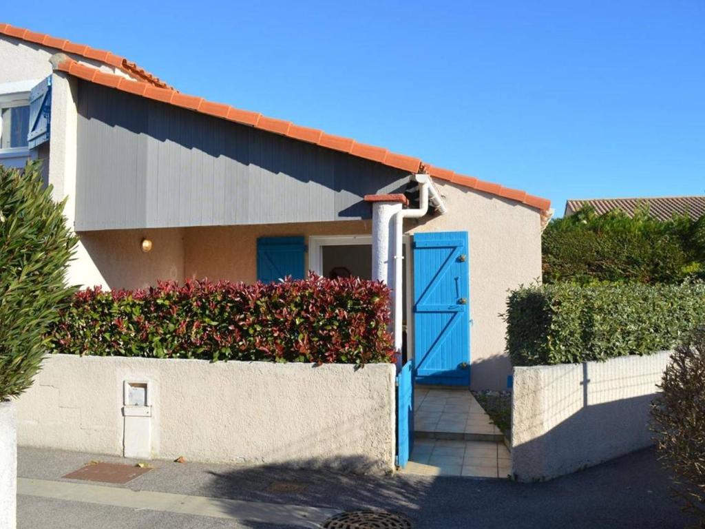 une maison avec une porte bleue et quelques buissons dans l'établissement Maison cosy avec mezzanine, terrasse, piscine et parking – Saint-Cyprien - FR-1-225D-558, à Saint Cyprien Plage