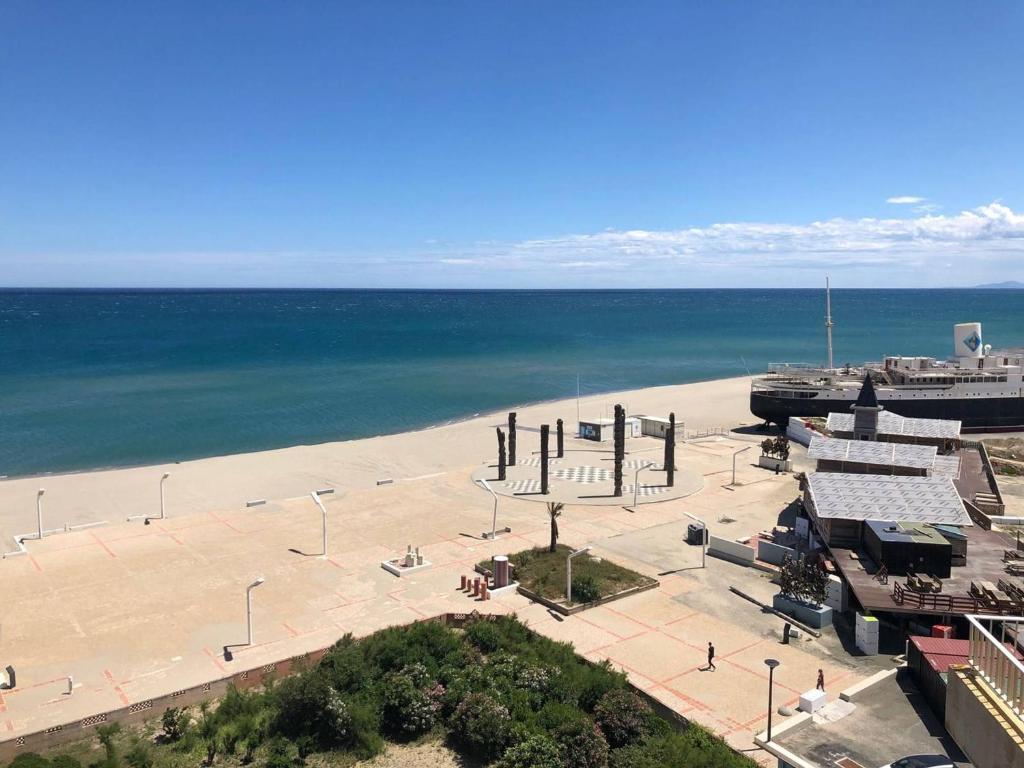 une vue d'une plage avec un bâtiment et l'océan dans l'établissement Appartement T3 climatisé avec 6 couchages, terrasse et parking à 300m des commerces - FR-1-81-490, au Barcarès
