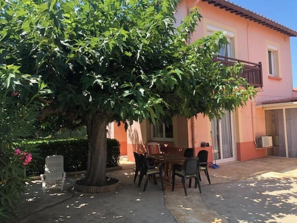 a table and chairs under a tree in front of a house at Villa T5 avec jardin, 100m plage, clim, WiFi, pour 8-10 pers, Le Barcarès - FR-1-81-524 in Le Barcarès