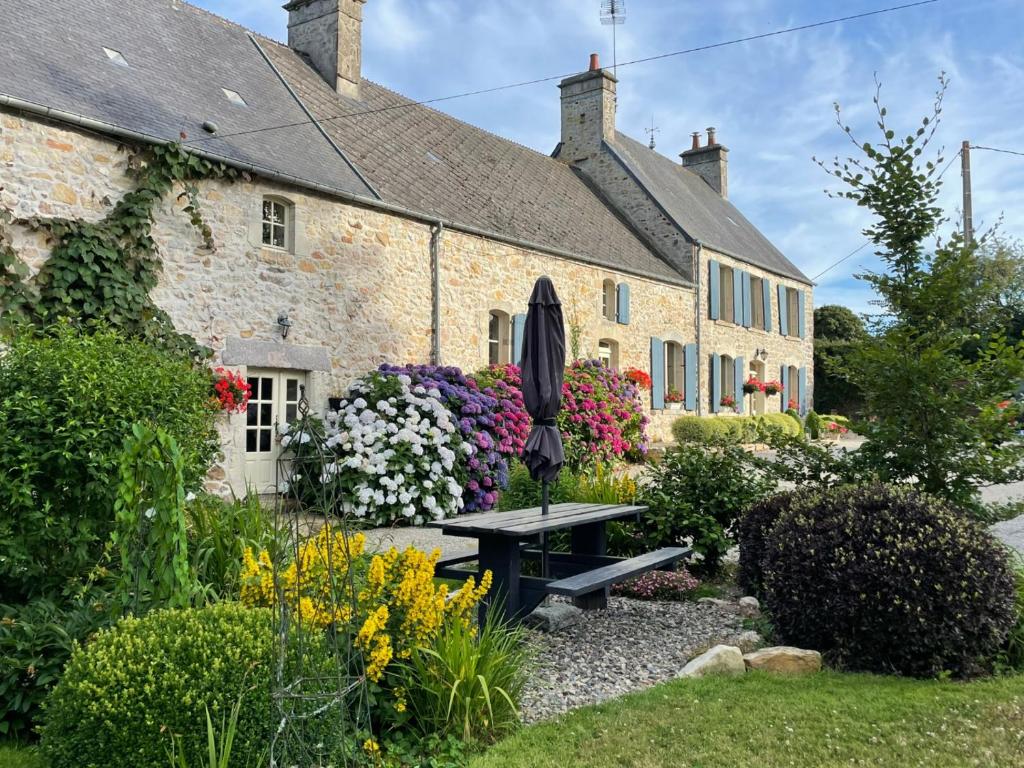 un jardin en face d'une maison en pierre avec un parasol dans l'établissement La Lande, à Bricquebec