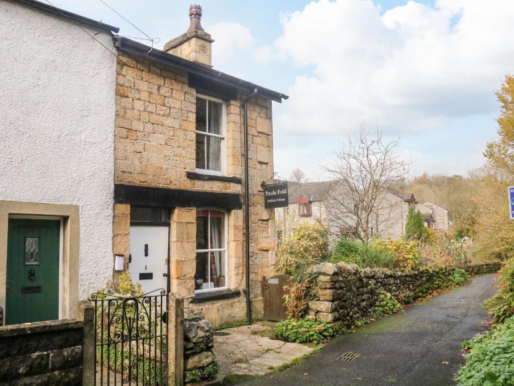 an old stone house with a green door on a street at Pauls Fold Holiday Cottage in Ingleton