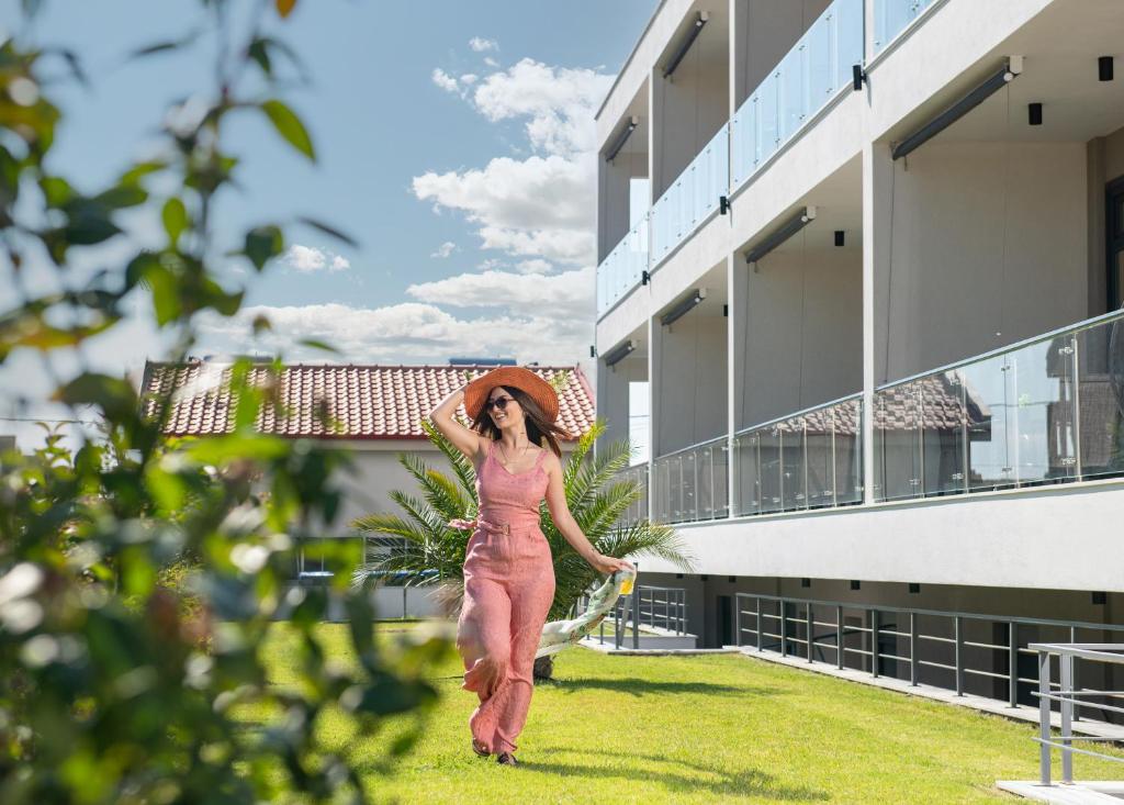 una mujer con un vestido rosa y sombrero caminando fuera de un edificio en San Giorgio Apartments Nikiti, en Nikiti