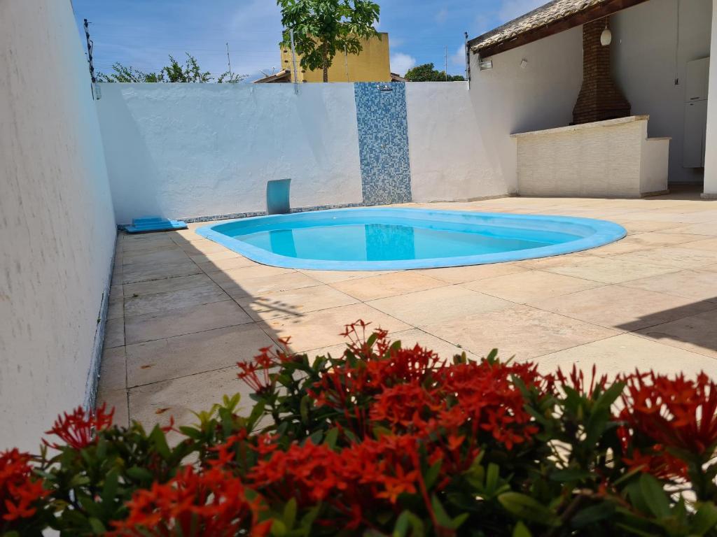 una pequeña piscina azul en un patio con flores rojas en Casa na Aruana com piscina e 3/4, en Aracaju