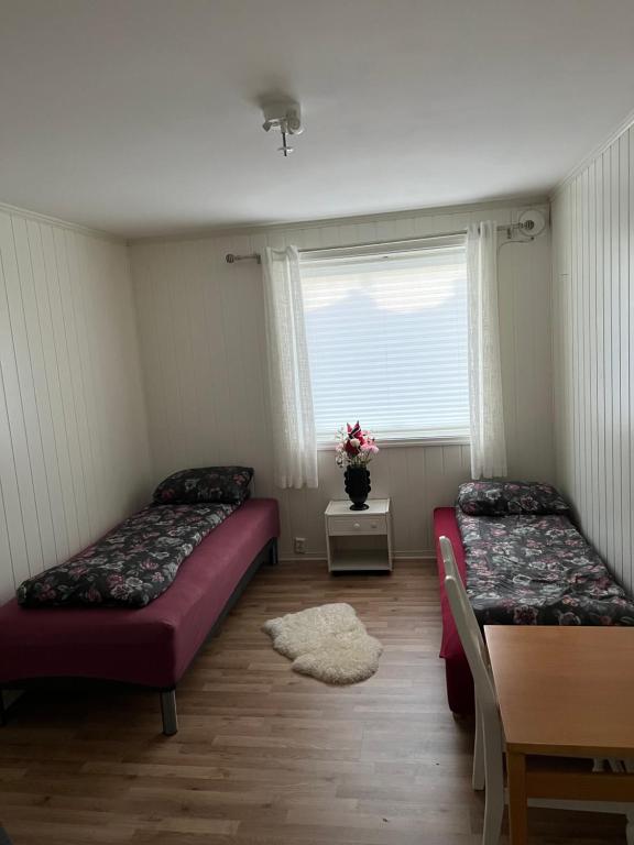 two beds in a room with a table and a window at Bedroom in city centre, no shower available in Ålesund
