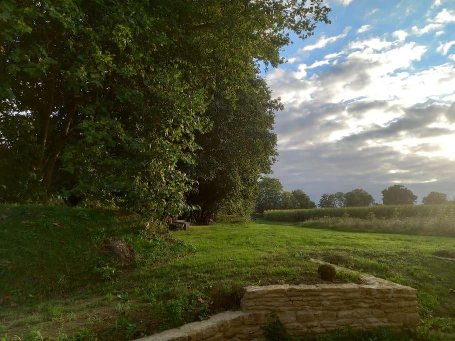 Un campo de hierba con árboles y un muro de piedra. en La Bergerie de Bénéauville 7 personnes, en Bavent
