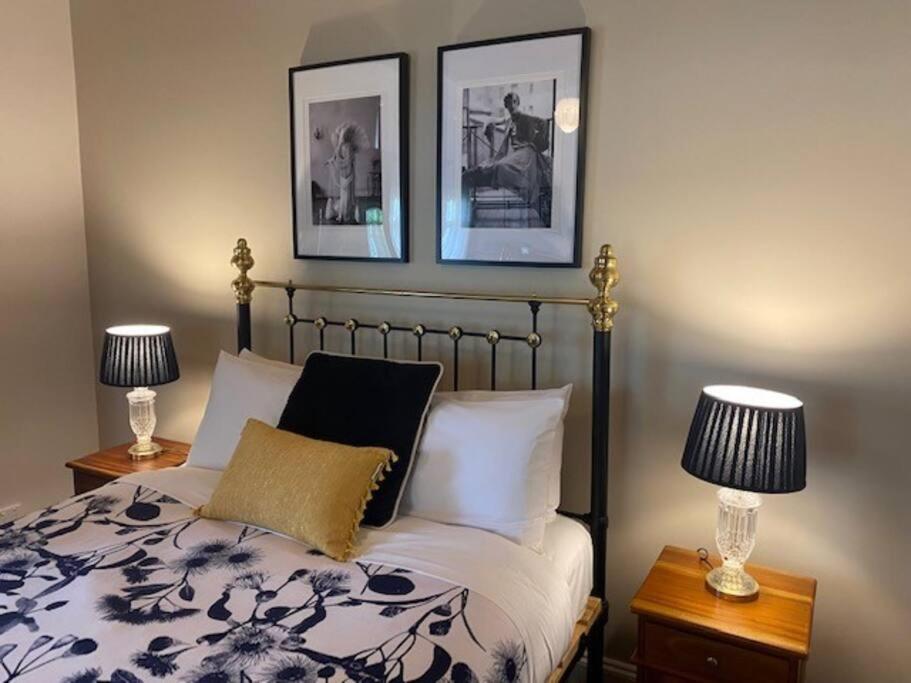 1 dormitorio con 1 cama con 2 lámparas y 2 cuadros en la pared en Glendale Cottage, en Daylesford