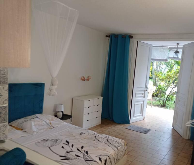 a bedroom with a bed and a blue curtain and a door at Charmant Studio à Sainte Anne -Plage avec Parking in Sainte-Anne
