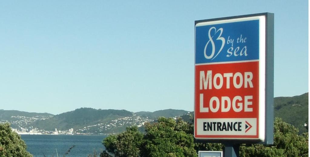 a sign for a motor lodge with the ocean in the background at ASURE 83 By The Sea Motor Lodge in Lower Hutt