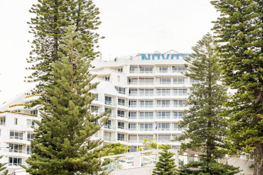 a large white building with trees in front of it at Novotel Sydney Brighton Beach in Sydney