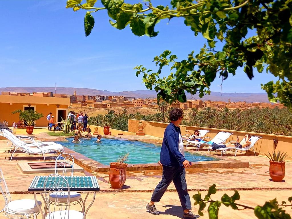 Un homme se promène au bord d'une piscine avec des gens dans l'établissement Auberge Kasbah Ennakhile, à Nkob