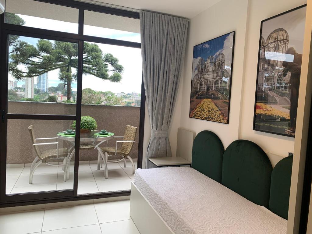 a room with a bed and a balcony with a table at Estúdio Lindíssimo com Varanda! in Curitiba