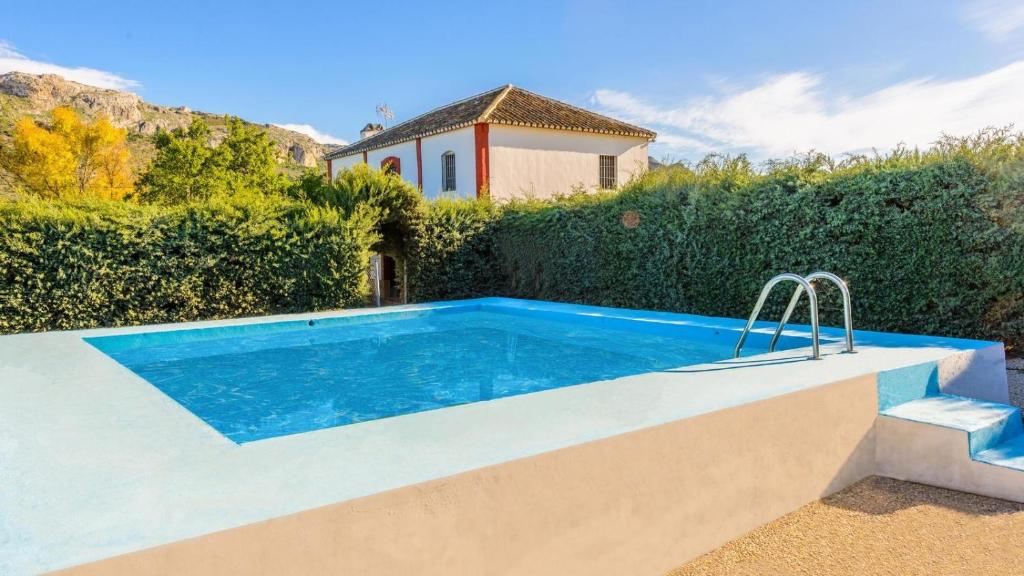 een zwembad voor een heg met een huis bij Huerta Nueva Cuevas del Becerro by Ruralidays in Cuevas del Becerro