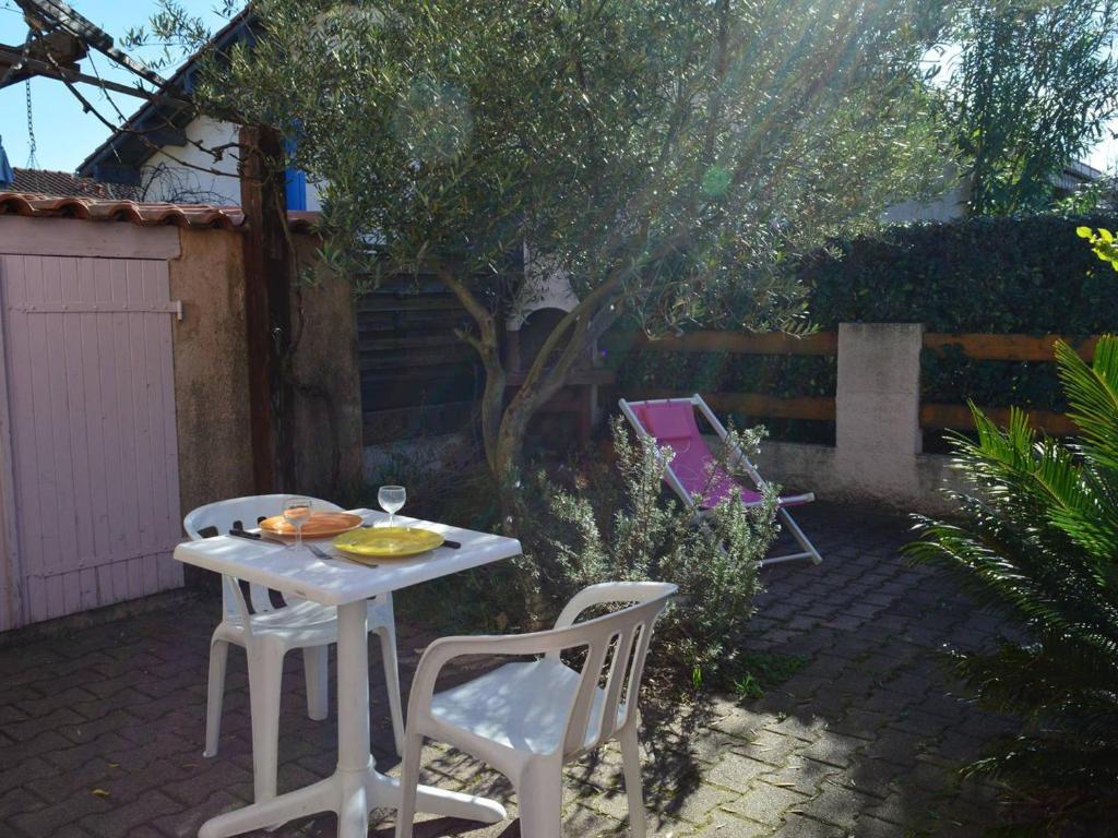 une table et des chaises blanches dans une arrière-cour avec un arbre dans l'établissement Maison avec Mezzanine: Confort, Terrasse & Proximité Plage à Argelès-sur-Mer - FR-1-225-42, à Argelès-sur-Mer