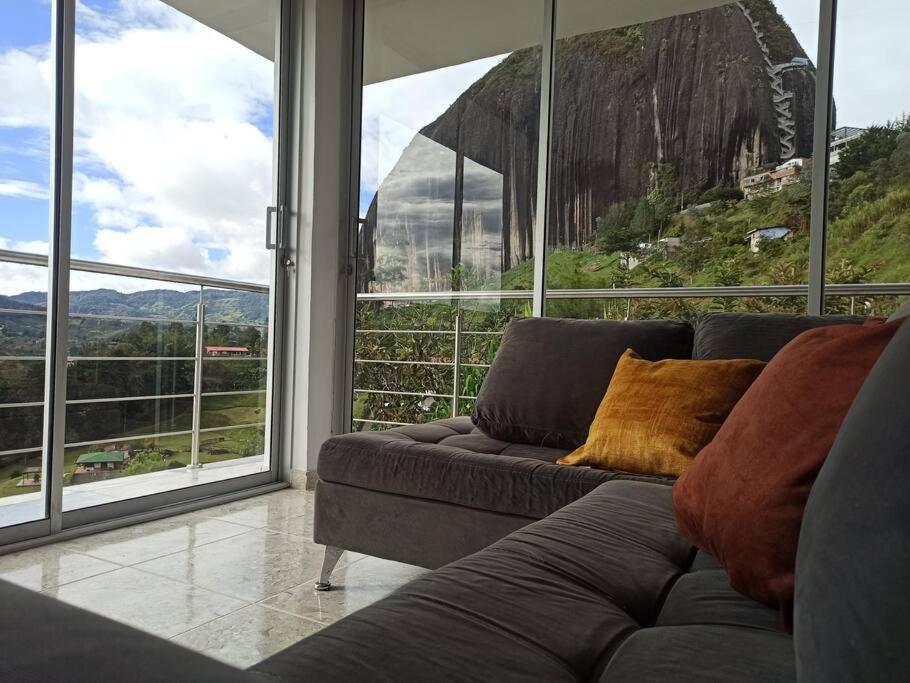 uma sala de estar com um sofá e janelas grandes em Linda casa con espectacular vista embalse y piedra em Guatapé