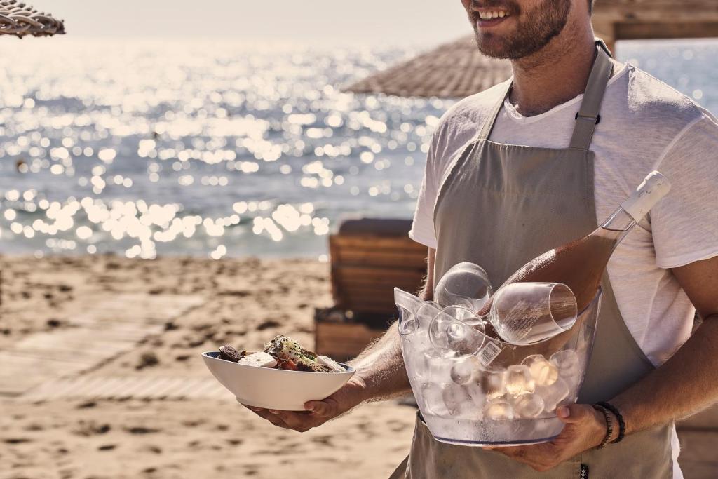 um homem segurando uma tigela de comida na praia em Dionysos Seaside Resort Ios em Mylopotas
