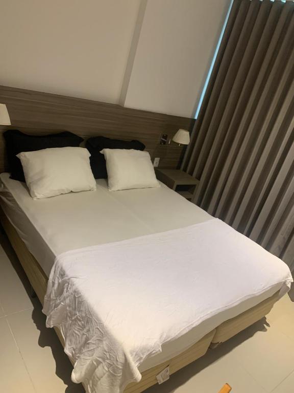 1 cama grande con sábanas y almohadas blancas en Flat completo com piscina, en Río de Janeiro