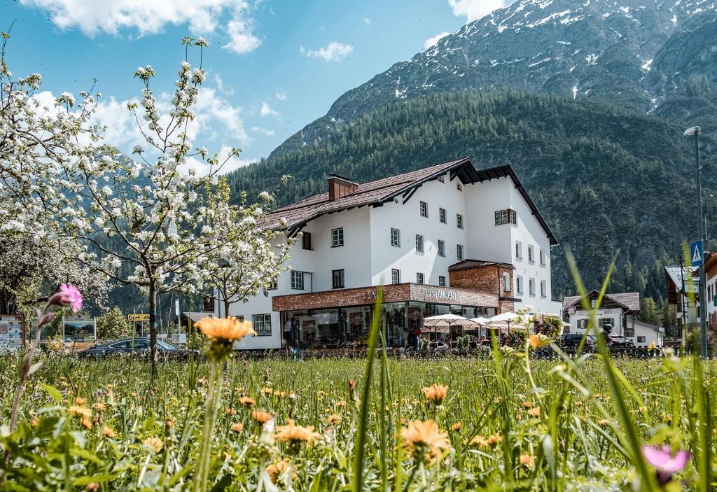 ein Gebäude auf einem Blumenfeld vor einem Berg in der Unterkunft Posthotel Lechtal in Holzgau