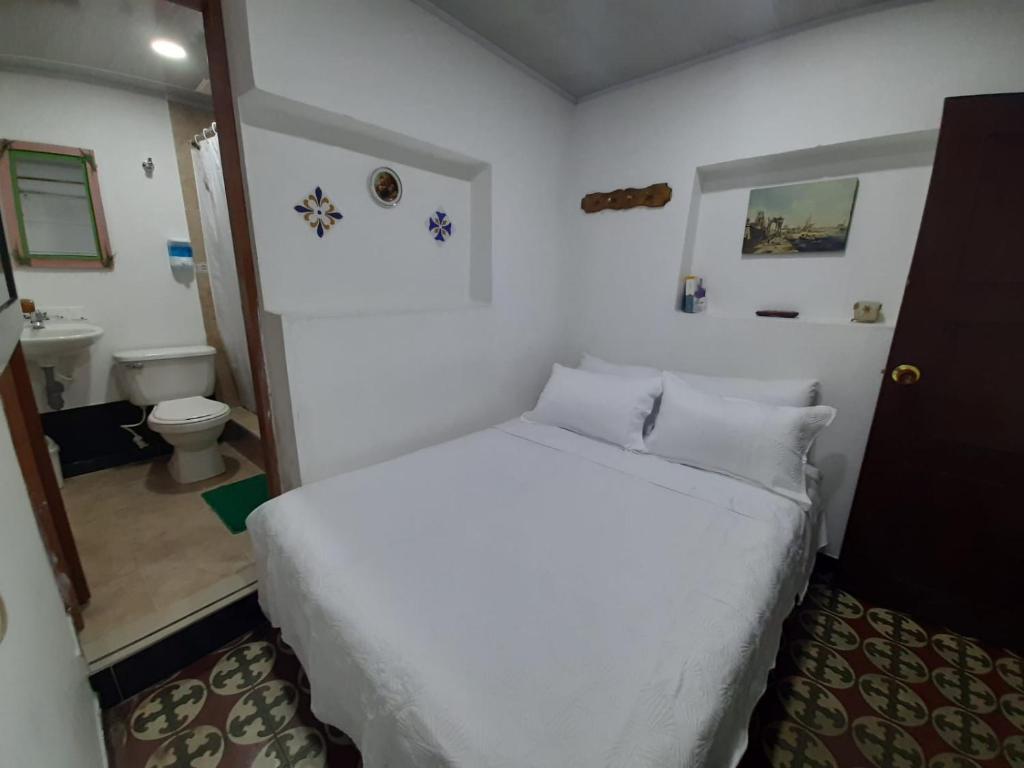 a bedroom with a white bed and a bathroom at Hotel Posada Turística la Ceiba in Vergara