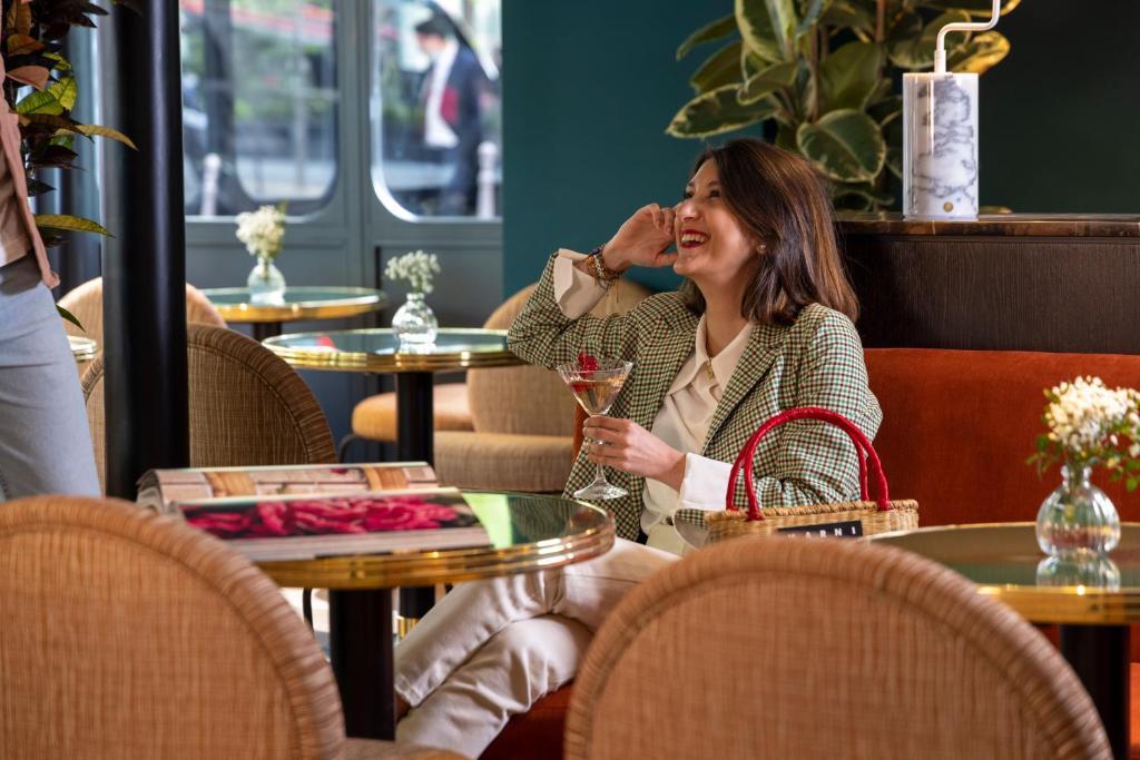 a woman sitting at a table with a glass of wine at Hôtel Toujours &amp; Spa in Paris