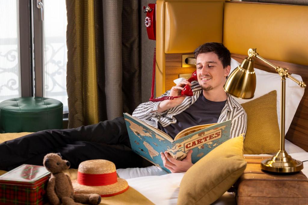 a man laying in bed reading a book at Hotel Whistler - Gare du Nord in Paris