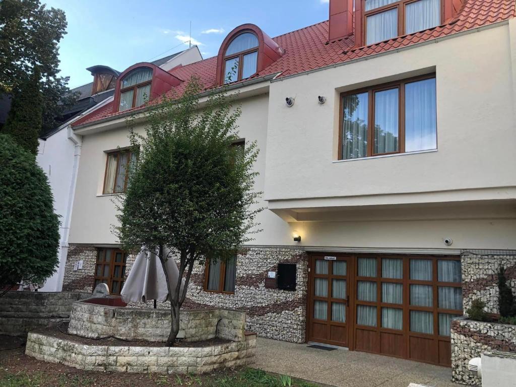 Una casa blanca con un árbol delante. en Atryum Hotel és Panzió en Szolnok