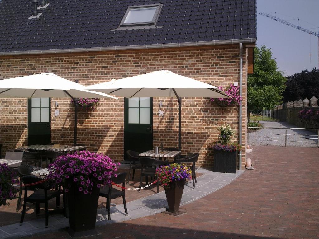 an outdoor patio with tables and umbrellas and flowers at B&B de Taller-Hoeve in Maasmechelen
