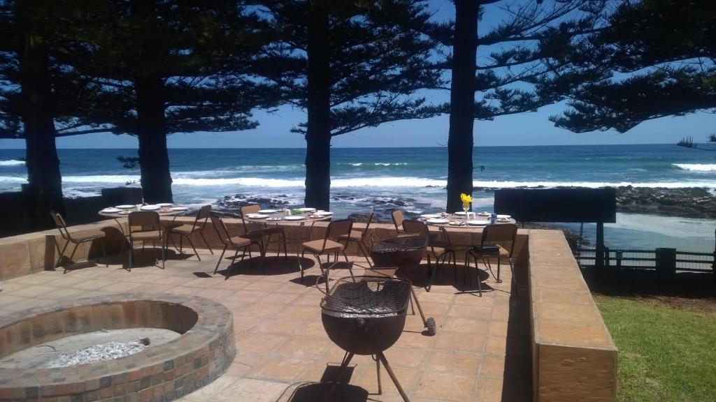 un patio con parrilla, mesas, sillas y el océano en Sea Otters Lodge, en Kini Bay