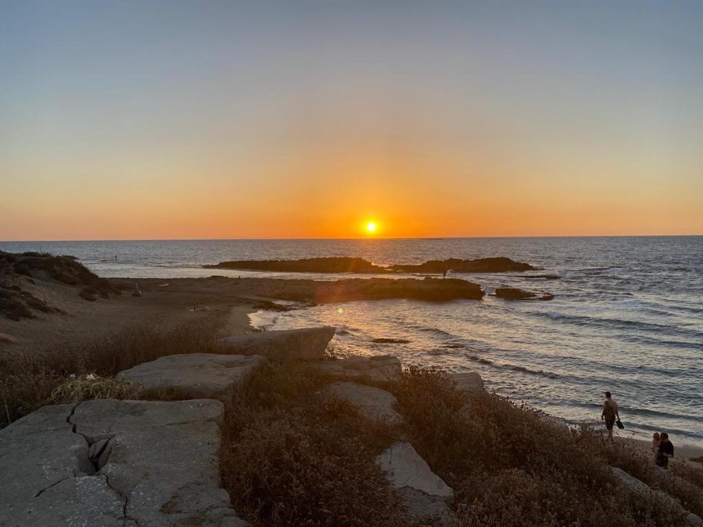 una puesta de sol sobre el océano con gente caminando por la playa en Sunset and sea view, wifi and more en Ashqelon