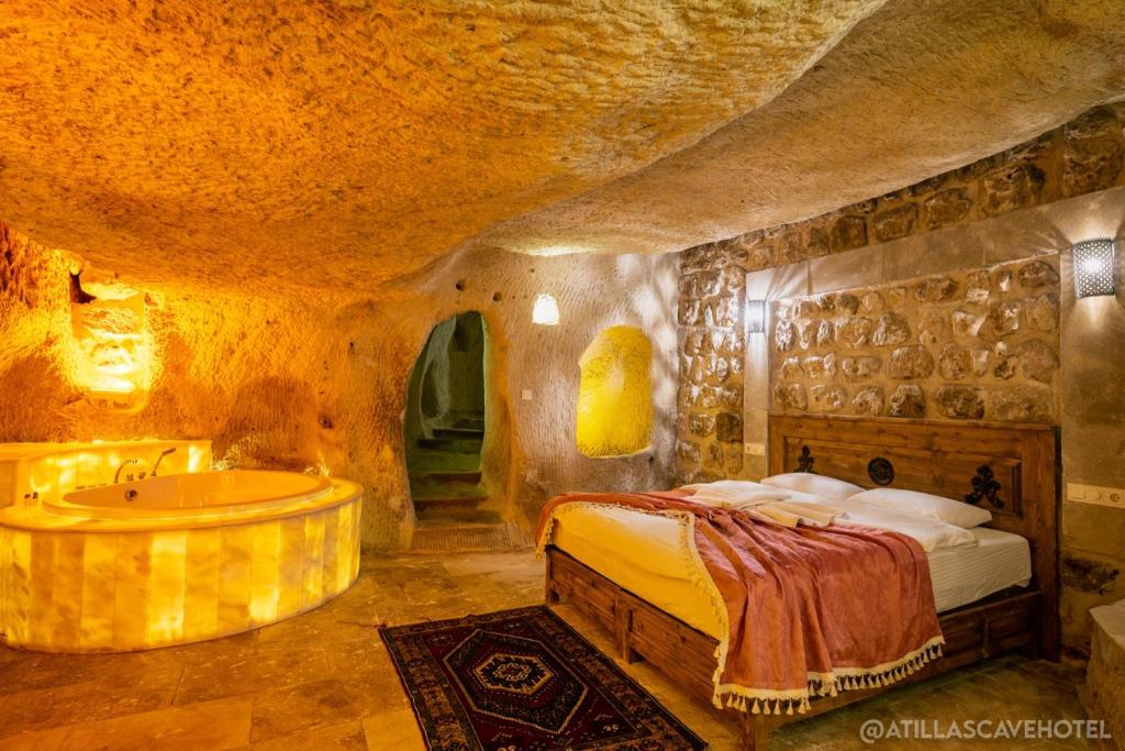 a bedroom with a bed and a tub in a cave at Atilla's Cave Hotel in Nevşehir