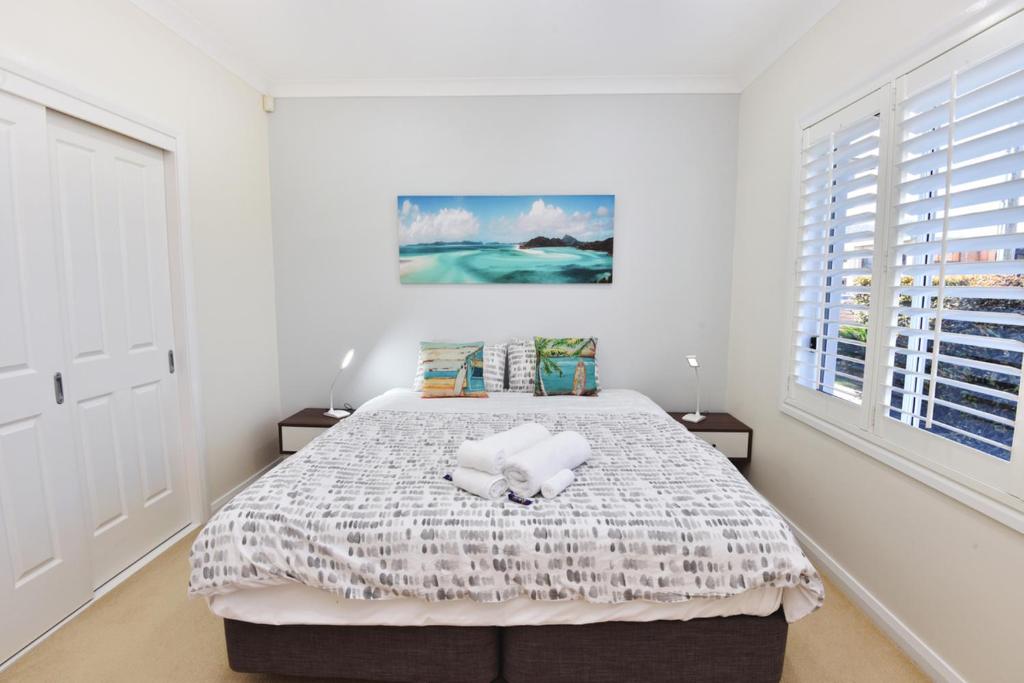a white bedroom with a large bed with two pillows at Point Bulli in Bulli