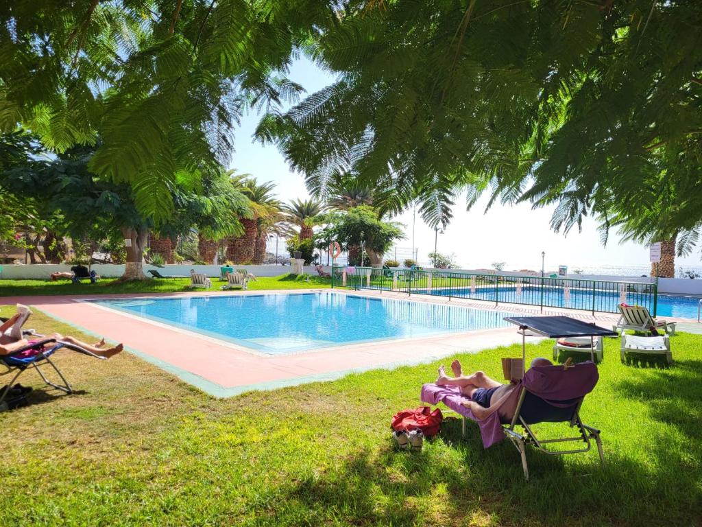 a group of people sitting in lawn chairs near a swimming pool at Paseo de Gracia - Lovely studio by the sea! in Los Cristianos