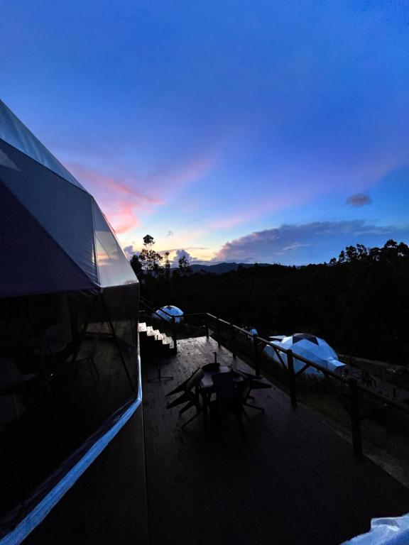 a building with a deck with a sunset in the background at Golden Glamping in Guatavita