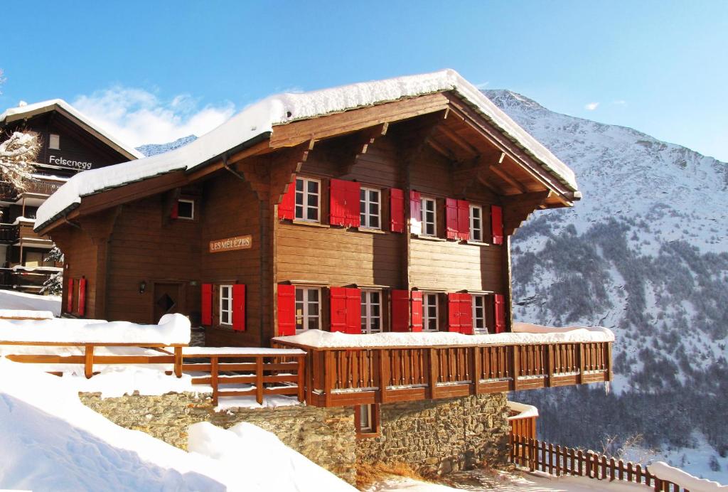 サースフェーにあるChalet Les Mélèzesの雪中の赤い扉のある木造家屋