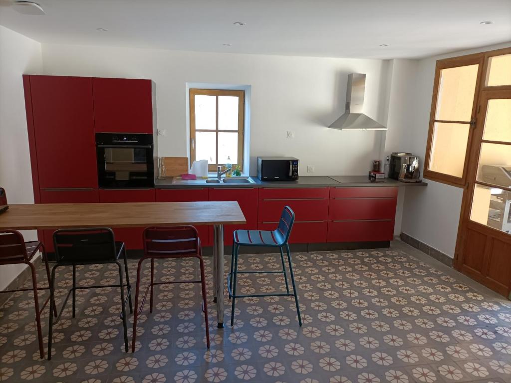 ラルジャンティエールにあるGrand Gîte terrasses Largentièreのキッチン(赤いキャビネット、木製テーブル、椅子付)