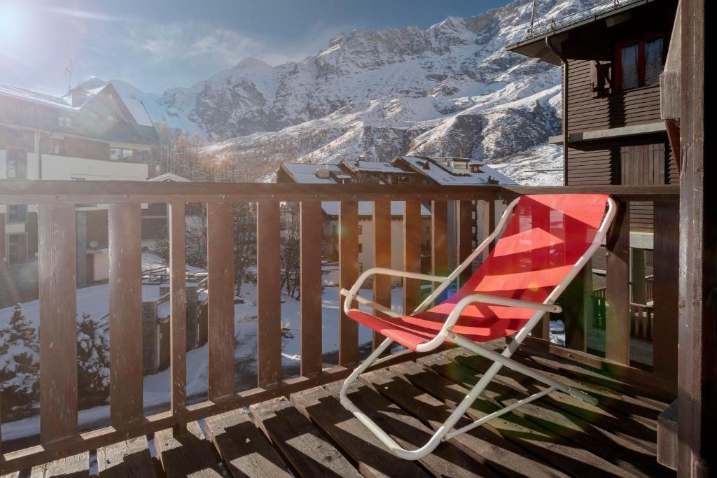 a red rocking chair sitting on a balcony with mountains at HelloChalet - Foyer du Cervin 250m skiruns in Breuil-Cervinia