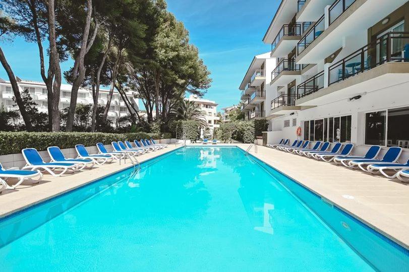 a swimming pool with lounge chairs and a building at Guya Wave Hotel in Cala Ratjada