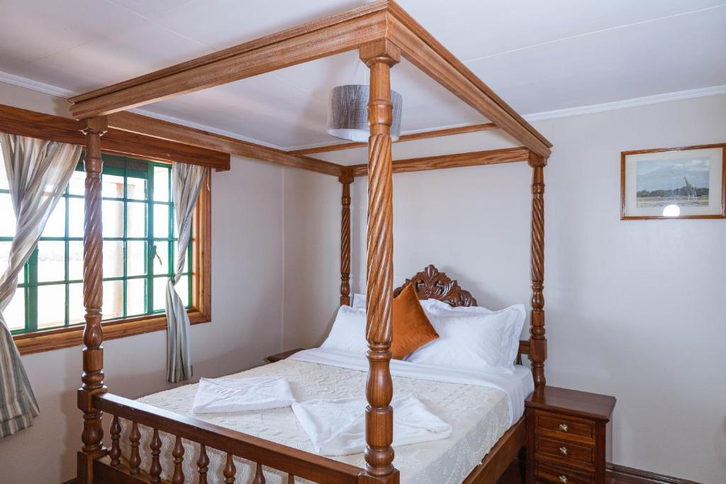a wooden four poster bed in a room with a window at Wild Amboseli Ndovu Cottage. in Amboseli