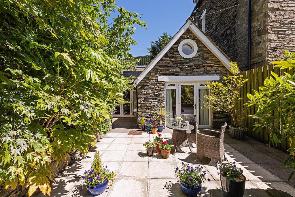 a stone house with a patio with chairs and flowers at Wheatlands Cottage in Windermere