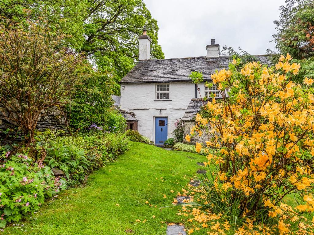 una antigua casa de campo blanca con una puerta azul en un jardín en Knotts Cottage, en Windermere