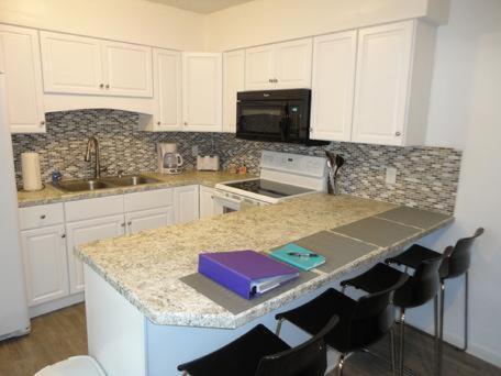 a kitchen with white cabinets and a counter top with chairs at Richard Arms Unit 15 in Cocoa Beach