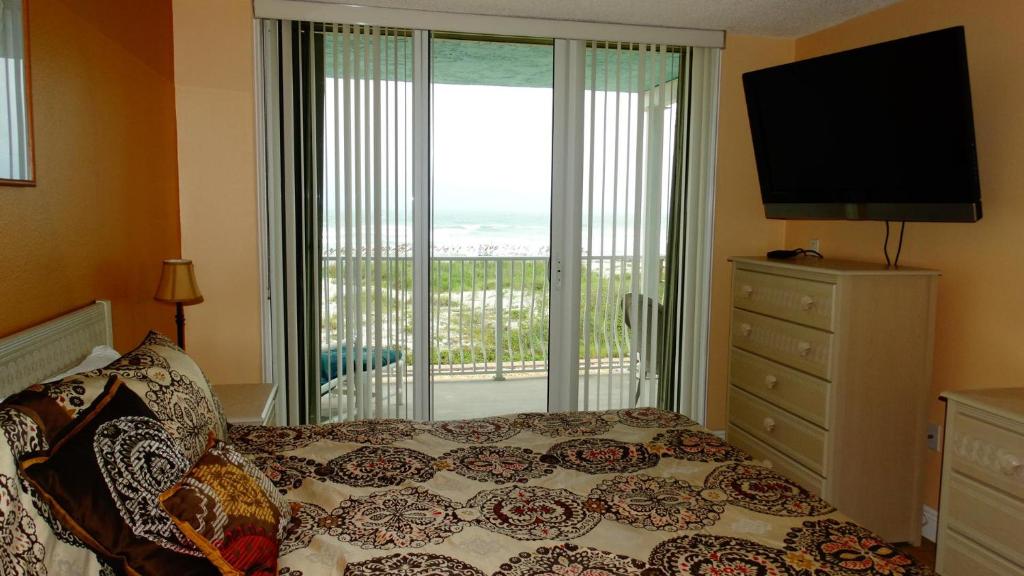 1 dormitorio con cama, TV y balcón en Ocean Beach Villas Unit 203- Direct Oceanfront Condo! en Cocoa Beach