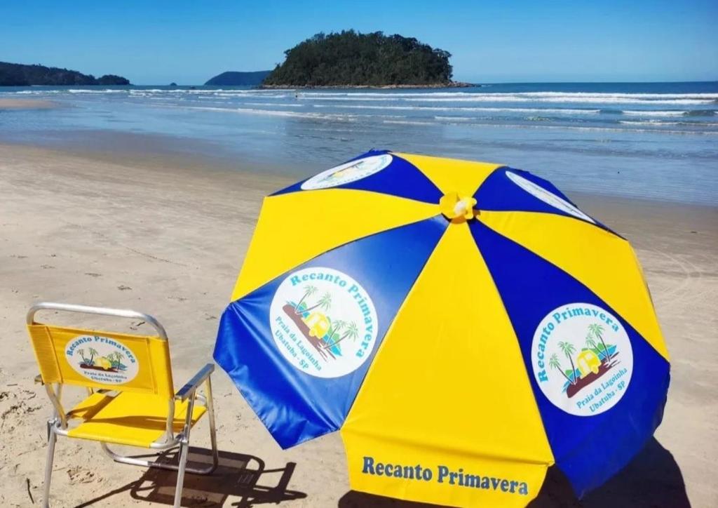 a yellow and blue umbrella and two chairs on a beach at Recanto Primavera Ubatuba in Ubatuba